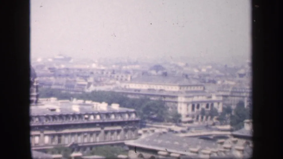 1949 French elevated city view with long grey rooflines, pale buildings, trees, haze, and dark foreground framing.