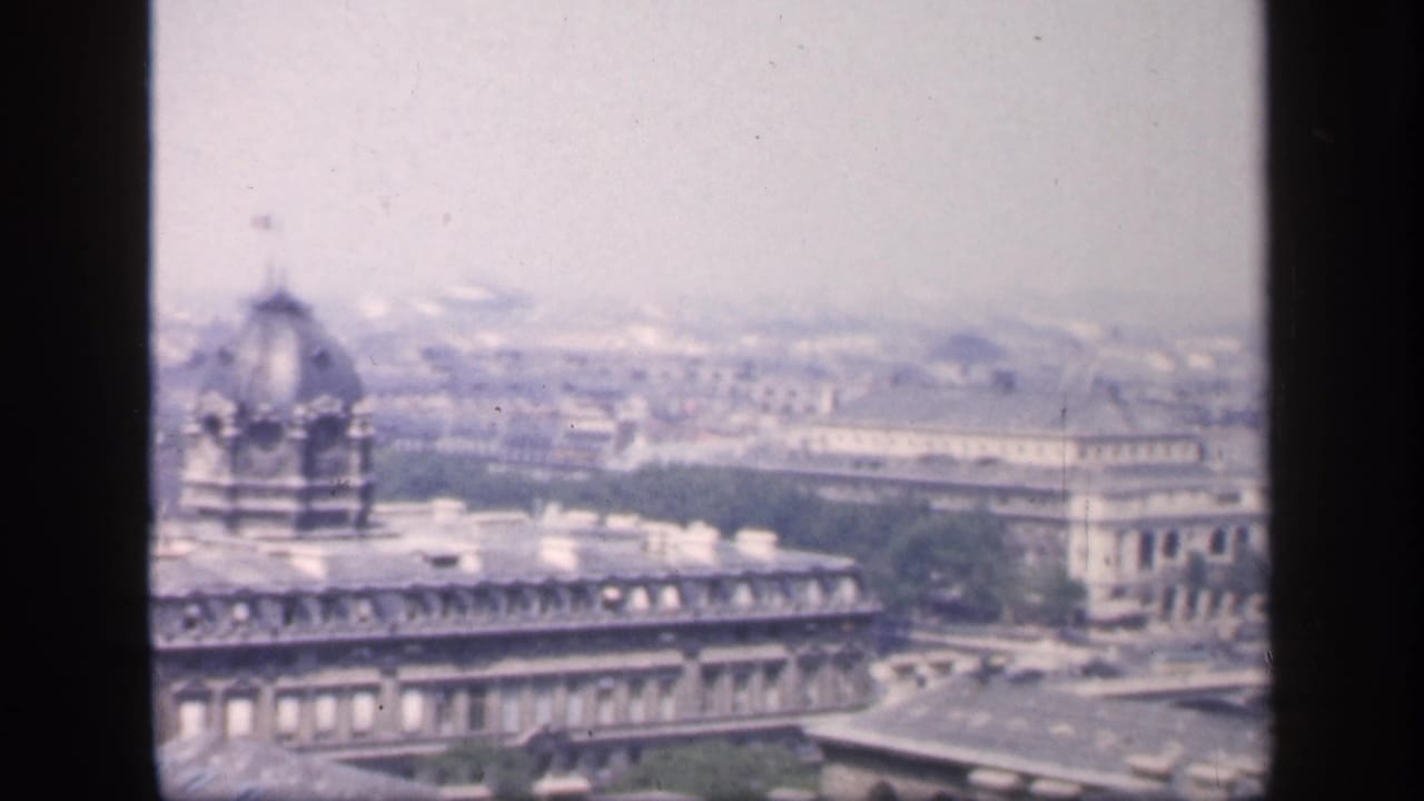 Soft elevated view across Paris rooftops with a domed structure and distant city haze.