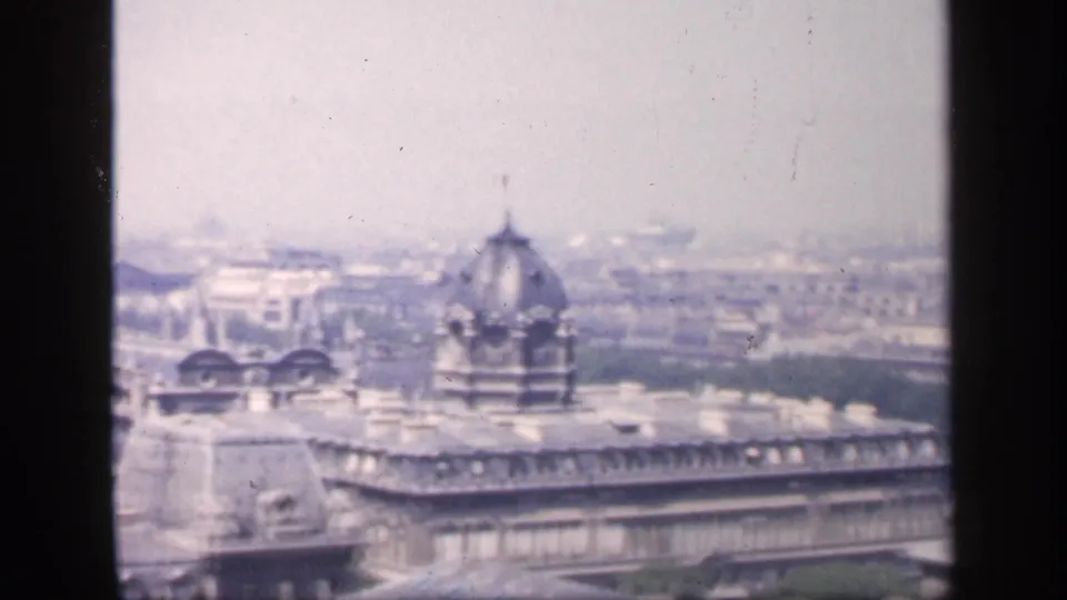 Mid-pan 1949 France frame with Parisian rooftops, a prominent dome, and distant urban blocks softened by haze.