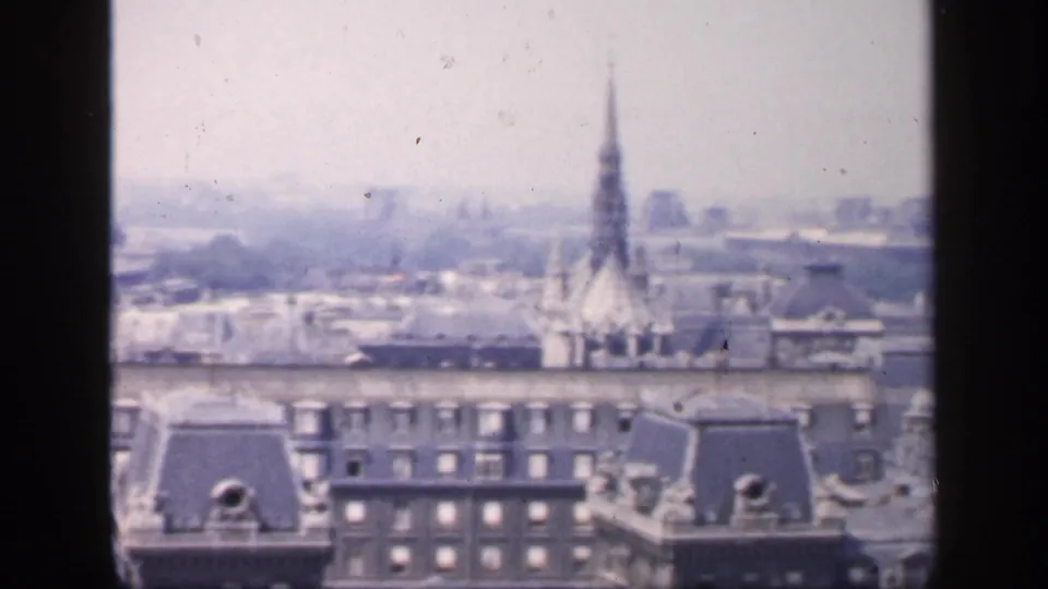 1949 France home-movie frame showing hazy Paris-like rooftops, dormers, chimneys and a distant spire above the skyline.