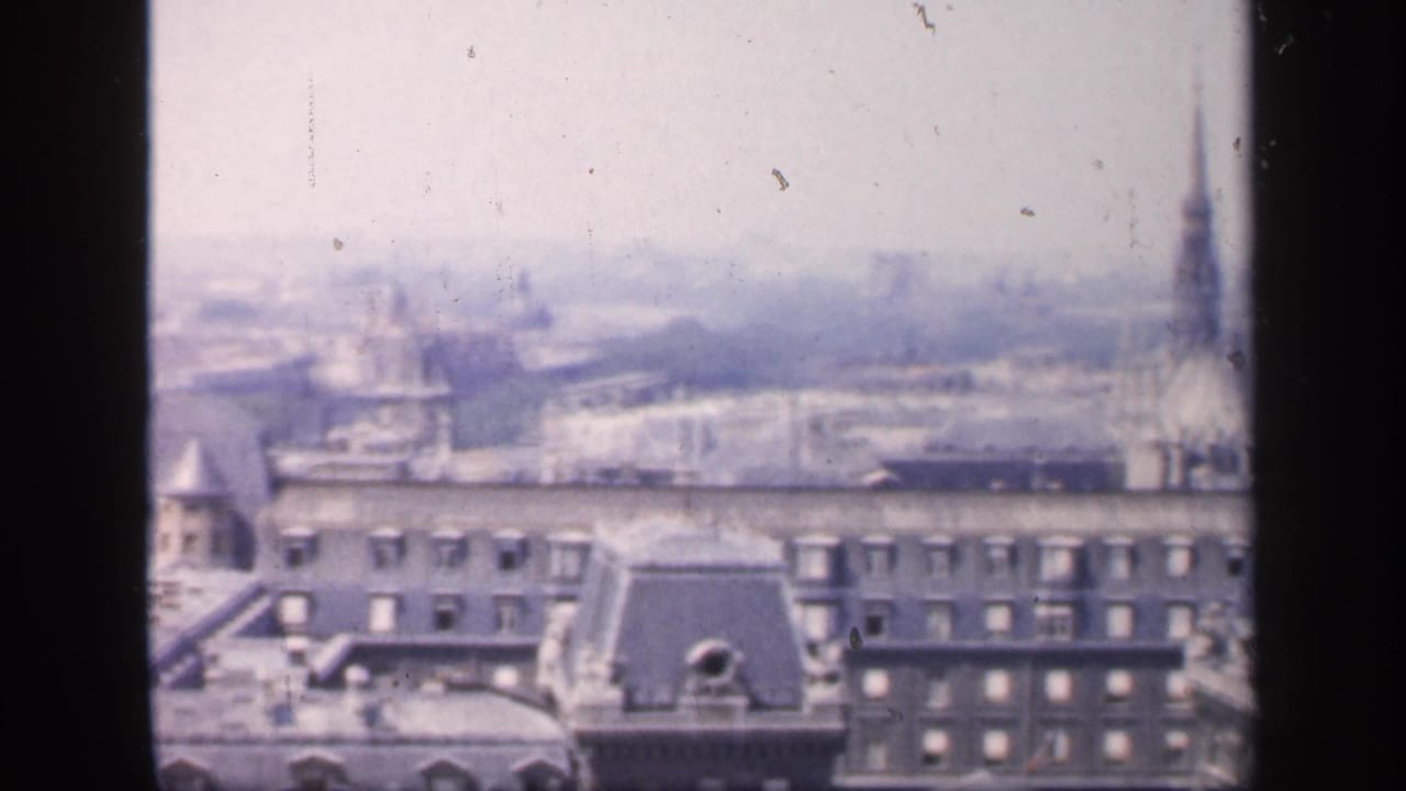 1949 France frame with dense rooftops, chimneys and faint distant tower forms across a soft, overexposed skyline.