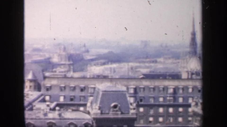 1949 France frame with dense rooftops, chimneys and faint distant tower forms across a soft, overexposed skyline.