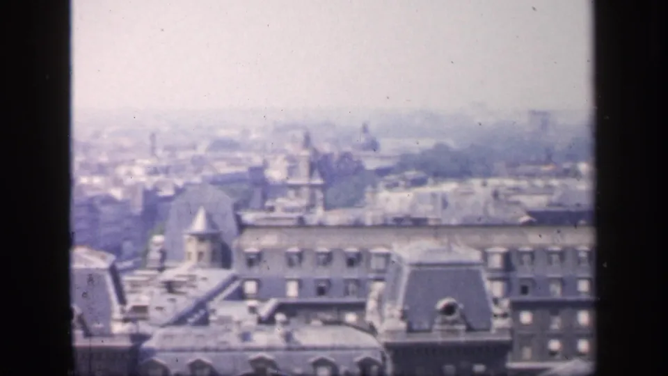 1949 France home-movie view over Paris-like rooftops, with dormers, a turret-like roof and pale city forms in haze.