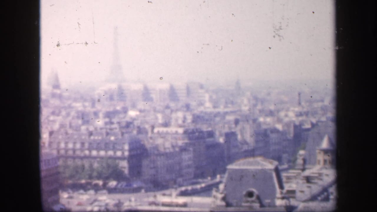 1949 8mm view over Paris, showing hazy rooftops, dense buildings, and a partial Seine bridge from an elevated vantage point.