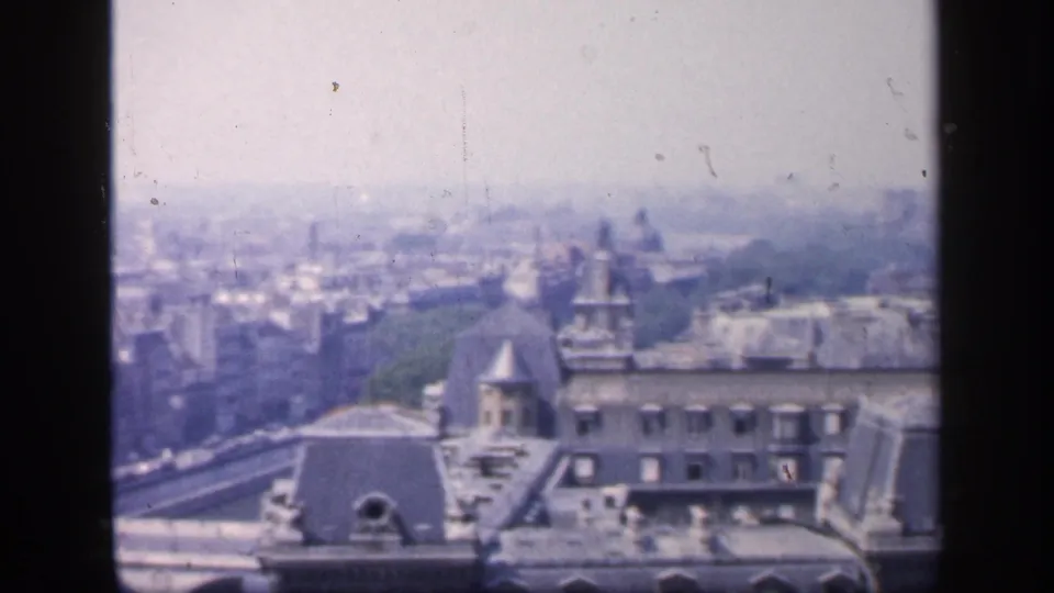 1949 8mm frame from a Paris panorama, showing rooftops, a bridge edge, distant landmark silhouettes, and a broad hazy skyline.