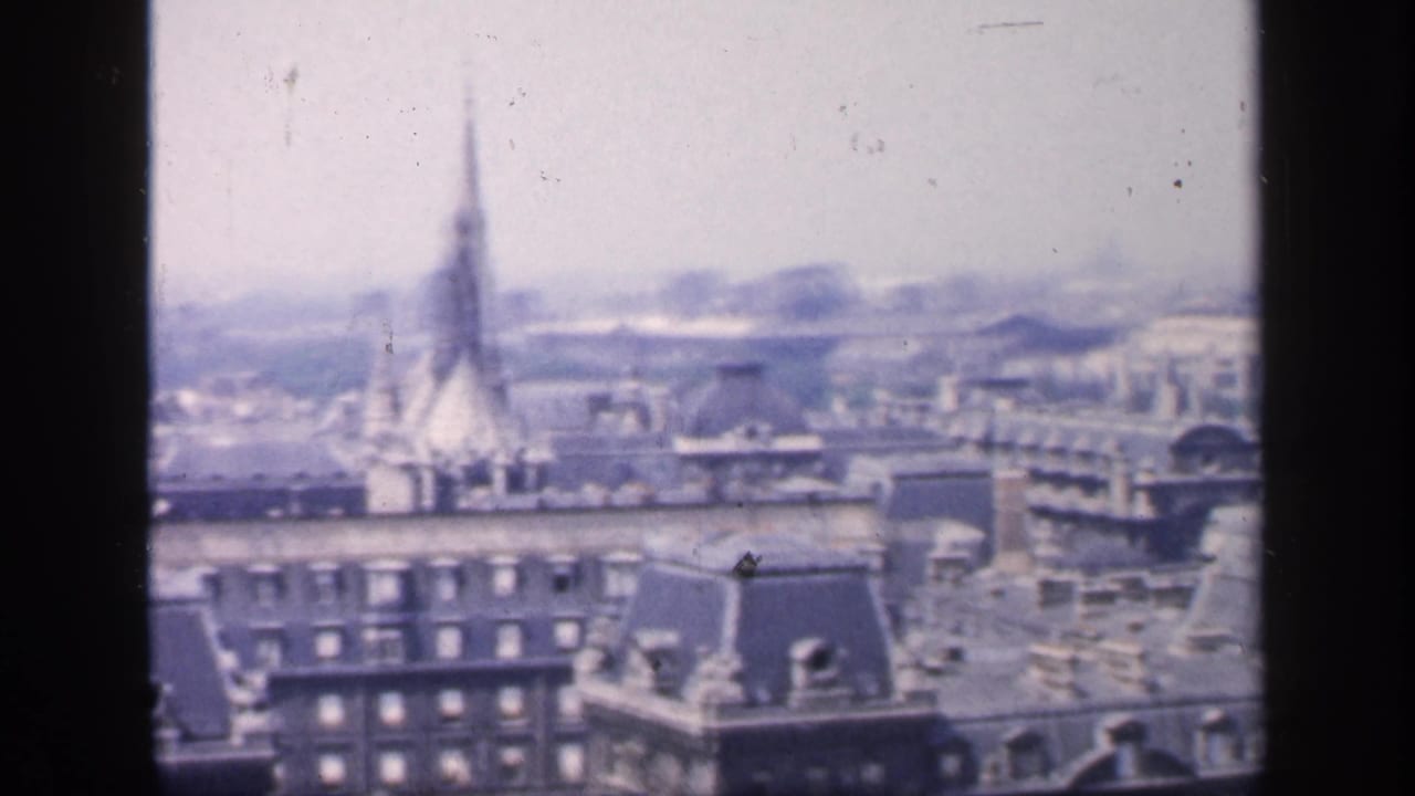 Soft-focus rooftops and a church spire seen from above with dark vertical film border.