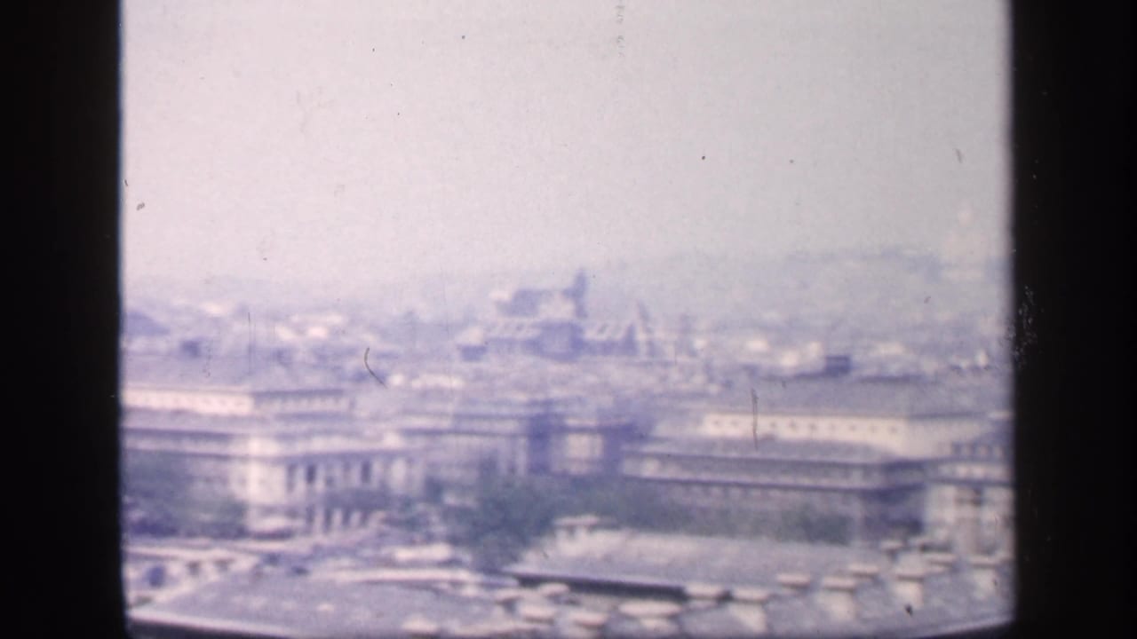 Elevated hazy city view with large buildings and rooftops beyond a dark film divider.