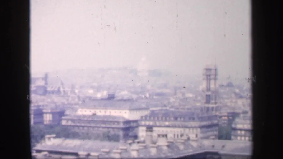 1949 New York City home-movie frame showing rooftops, a large building facade, and a tall tower or scaffold in the distance.