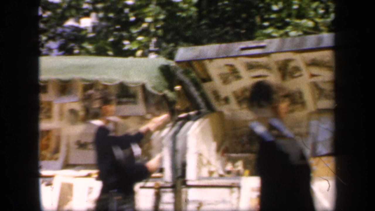 Outdoor photo display seen through dark framing with blurred pedestrians passing in front.