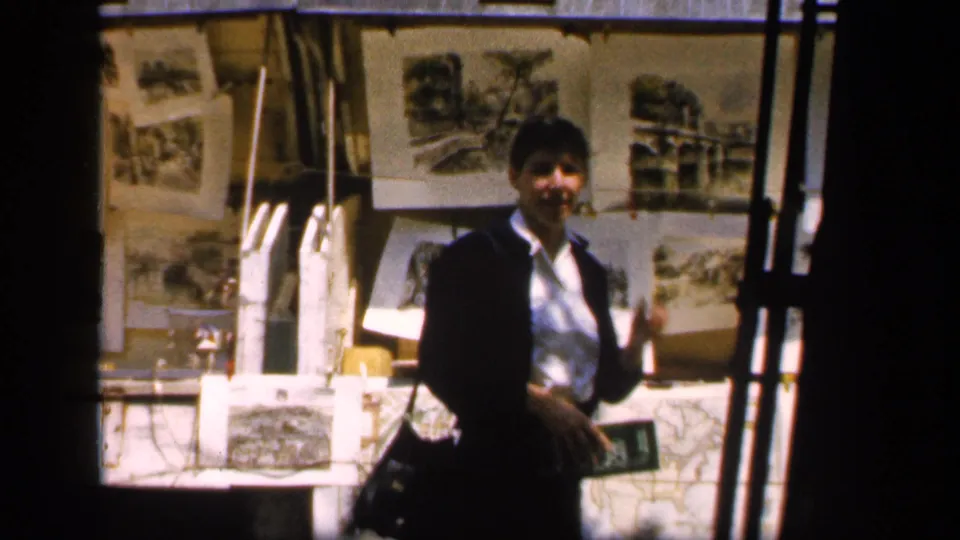 A person in dark clothing turns toward the camera near an outdoor display of photographs and drawings in 1949 France.
