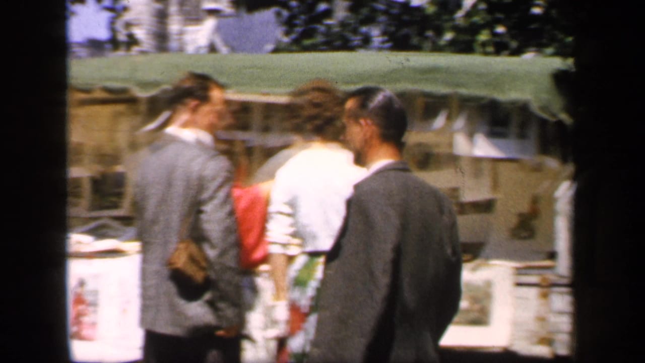 Several adults stand near outdoor picture stalls with framed works on display.
