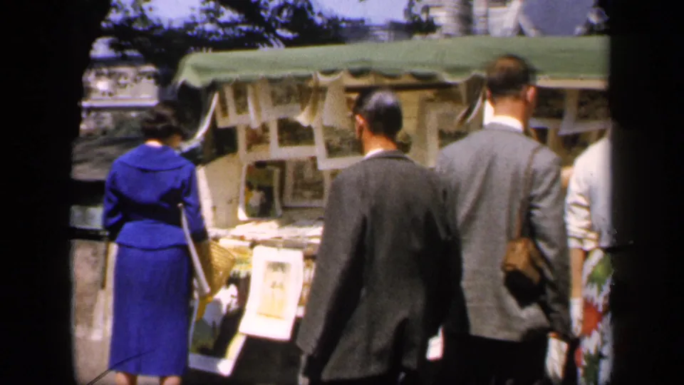 A small group faces outdoor picture stalls, including a woman in a blue dress and men in suits, in 1949 France.