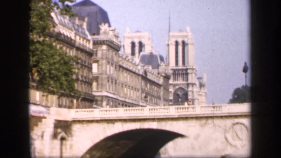 Notre-Dame Cathedral appears beyond a stone bridge and surrounding Paris buildings, seen from a visitor-shot 8mm view.