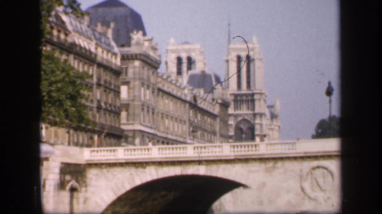 1949 Paris home-movie view of Notre-Dame Cathedral rising behind a stone bridge and adjoining riverside architecture.