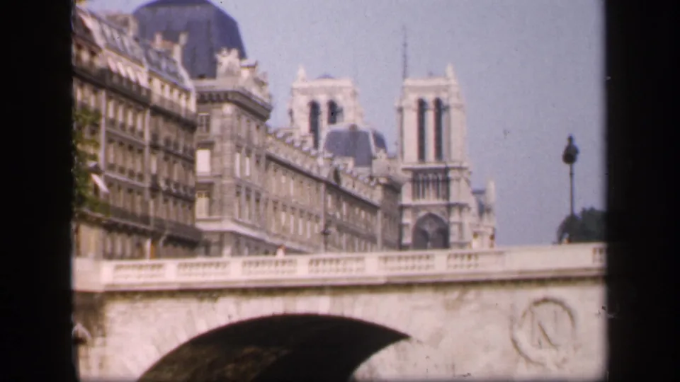 1949 France footage frames Notre-Dame Cathedral behind a bridge, with Haussmann-style facades along the river.