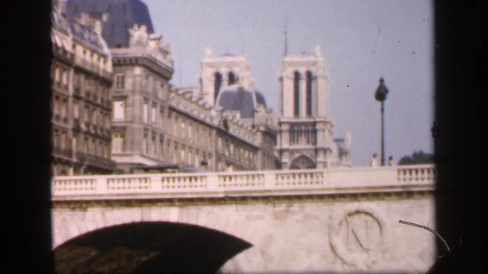 1949 Paris landmark view with Notre-Dame Cathedral behind a stone bridge, framed by soft 8mm film edges.