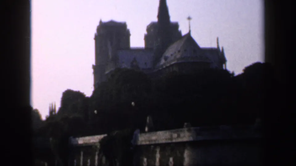 1949 Paris home-movie frame showing Notre-Dame in dark silhouette, with the roofline, towers, and spire partly obscured by trees.