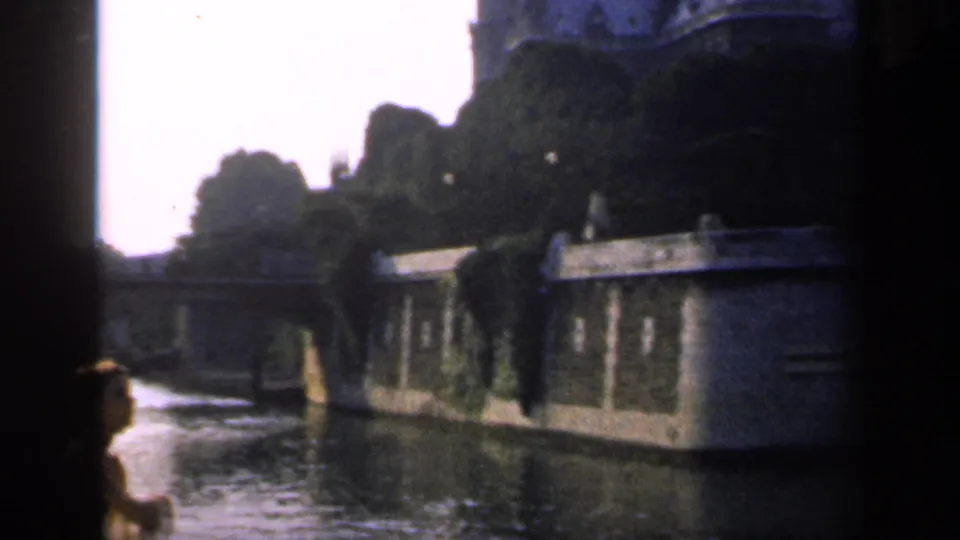 1949 France travel frame with a partially silhouetted foreground person looking across water toward masonry walls and trees.