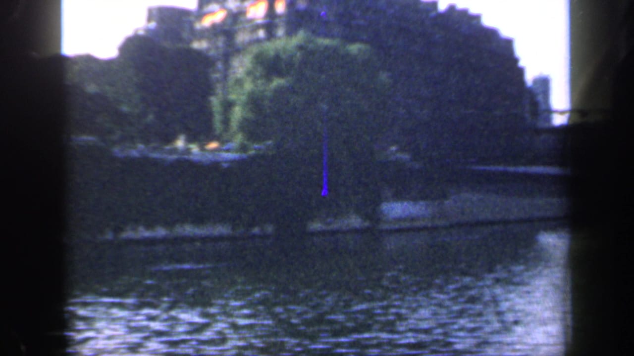 1949 France 8mm frame showing a river, tree-lined bank, distant buildings, and bridge elements seen through dark contact-sheet borders.