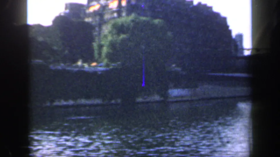 1949 France 8mm frame showing a river, tree-lined bank, distant buildings, and bridge elements seen through dark contact-sheet borders.