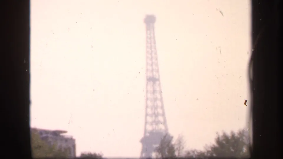 1949 France 8mm frame showing the Eiffel Tower in haze above trees and low buildings, bordered by dark film edges.