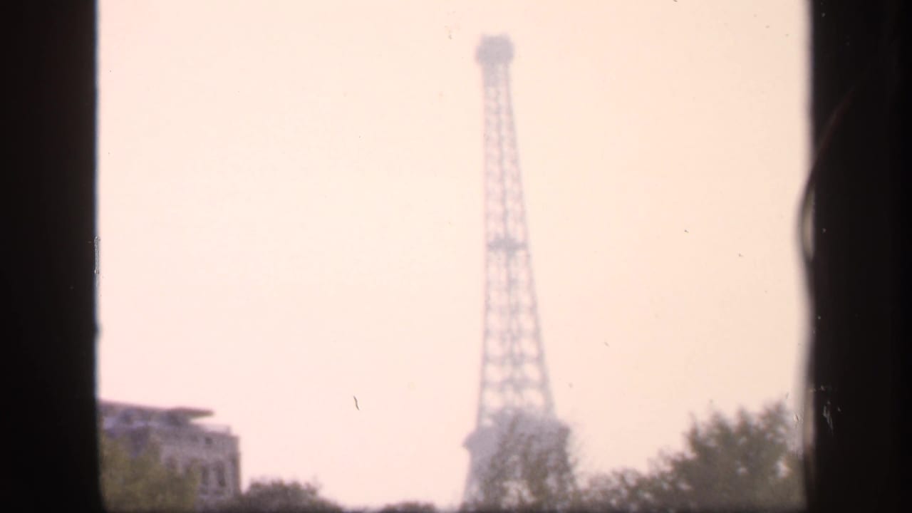 Distant Eiffel Tower seen through dark vertical borders with treetops below.