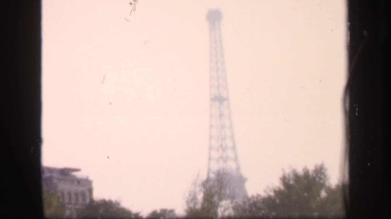 Hazy Eiffel Tower centered beyond trees and a partial building edge.