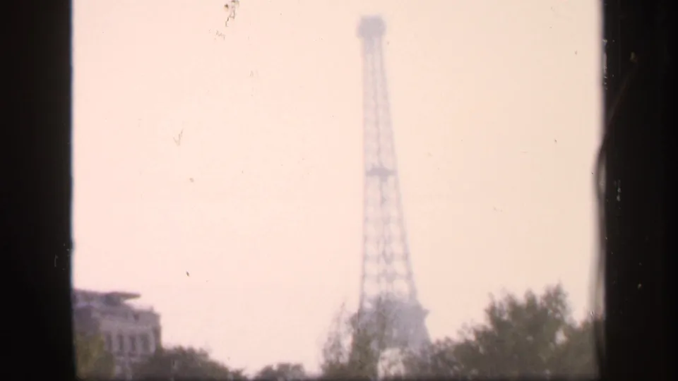 Distant Eiffel Tower in a hazy 1949 France travel frame, with dark window borders and treetops in the foreground.