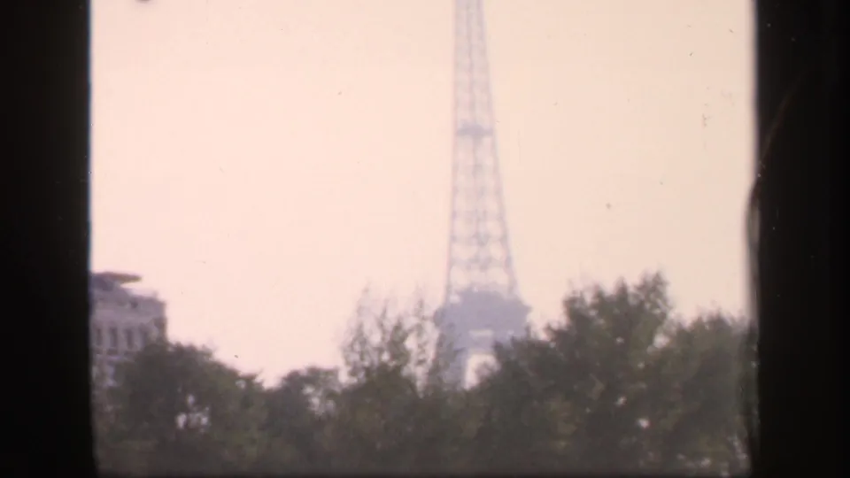 1949 France 8mm frame with the Eiffel Tower partly softened by haze above foreground trees and a shaded frame edge.