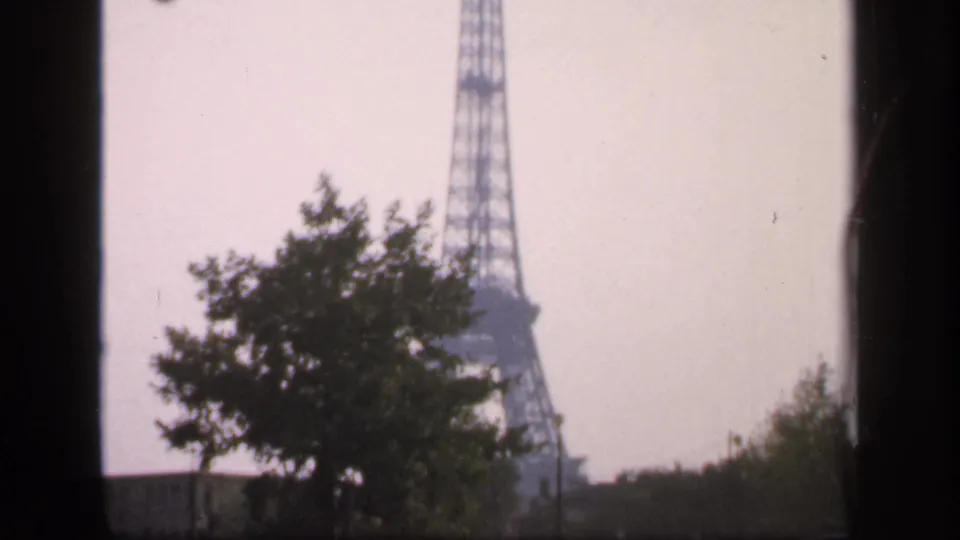 1949 France home-movie frame showing the Eiffel Tower shifted right, with a silhouetted tree and hazy sky in front.