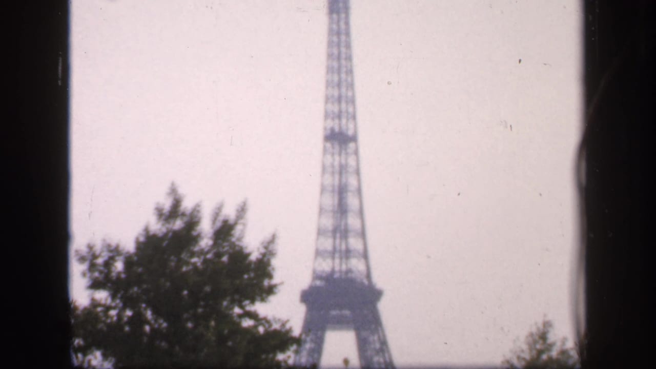 Eiffel Tower centered beyond trees with dark frame borders.
