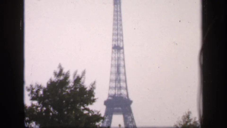 The Eiffel Tower stands beyond tree canopies in a muted 1949 Paris travel-film frame.