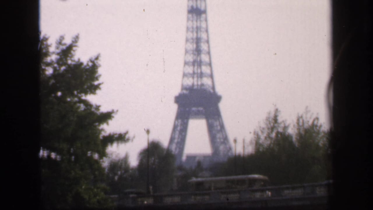 Distant Eiffel Tower seen beyond trees with a dark vertical frame edge.