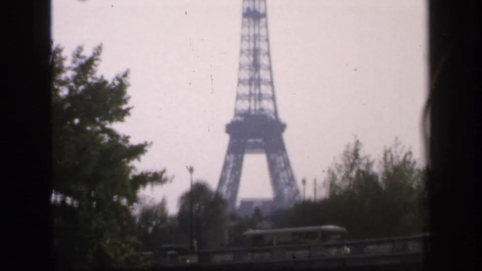 1949 Paris home-movie view of the Eiffel Tower in the distance, partly framed by trees and dark film borders.
