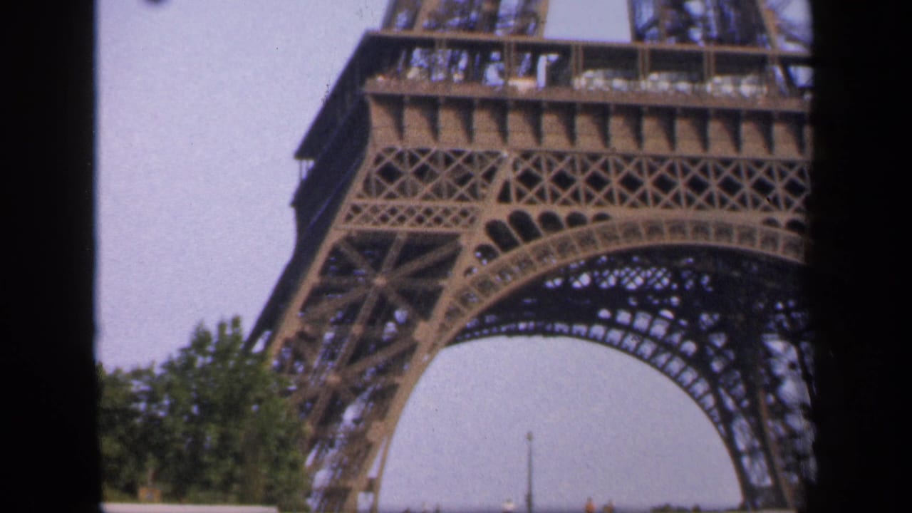 Close view of the Eiffel Tower base and lower arch against a pale sky.
