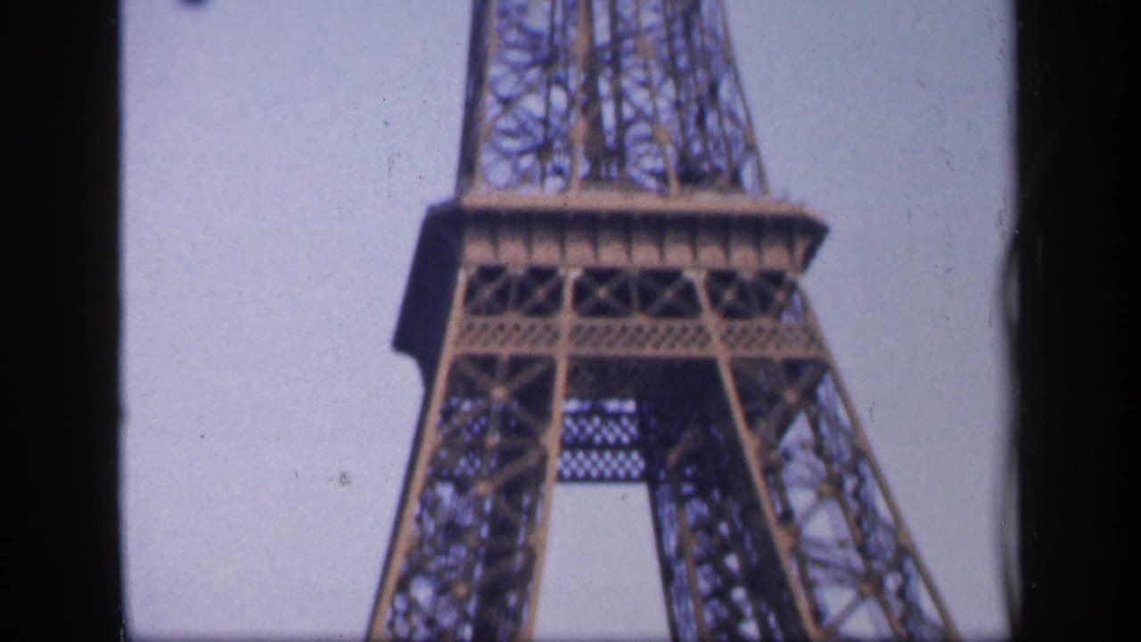 Upper and midsection of the Eiffel Tower against a pale sky.