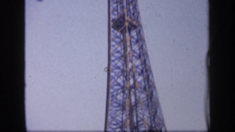 Vertical 8mm frame of the Eiffel Tower narrowing upward in Paris, with the structure partially cropped by the film edge.