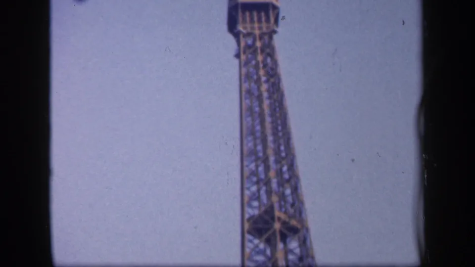 1949 home-movie view of the Eiffel Tower seen from below, with the tower centered vertically against a clear pale sky.