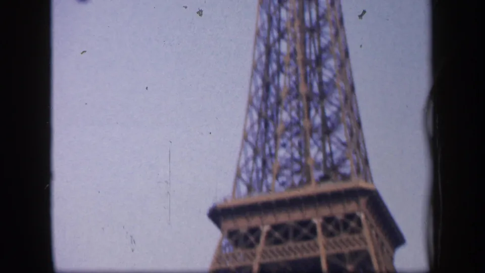 1949 Paris home-movie frame showing the Eiffel Tower midsection and platform in soft, grainy 8mm color.