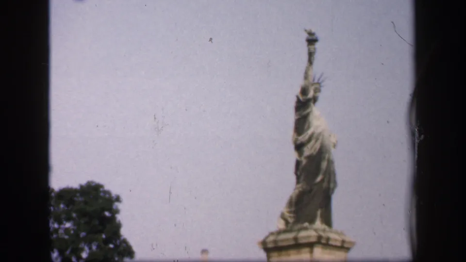 1949 New York home-movie frame showing the Statue of Liberty from the upper pedestal upward, with nearby foliage and visible 8mm film borders.