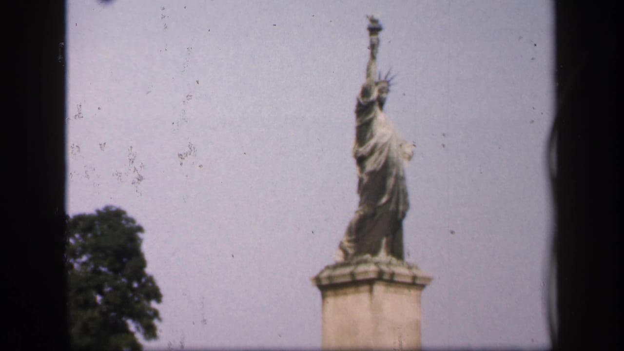 Small Liberty statue replica centered above a stone pedestal with sky and tree behind it.