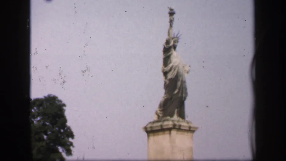 1949 8mm New York City frame of a small Statue of Liberty replica, with crown, torch, pedestal, and tree visible.
