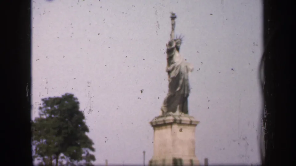 1949 8mm New York City frame of a small Statue of Liberty replica standing on a pedestal with trees at the edge of the shot.