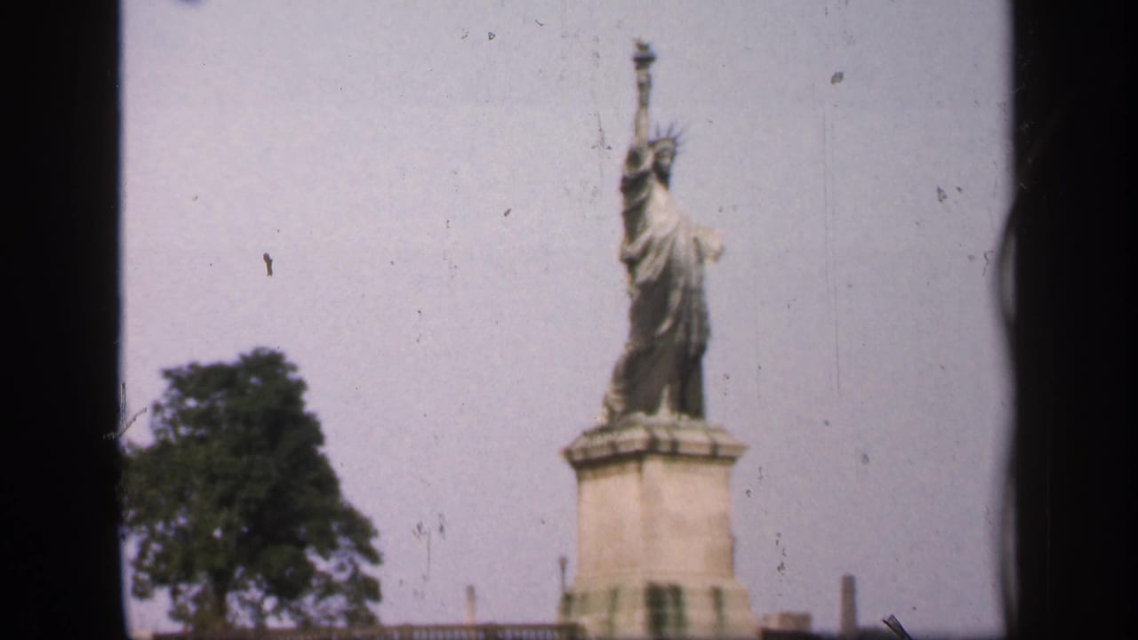 1949 France 8mm frame showing a Statue of Liberty replica on a riverside pedestal with trees and soft faded color.