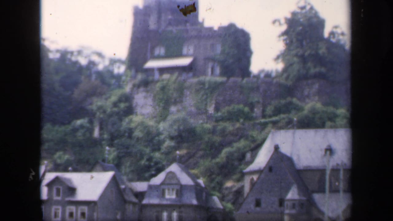 Hilltop stone structure and village houses framed by dark film edges.