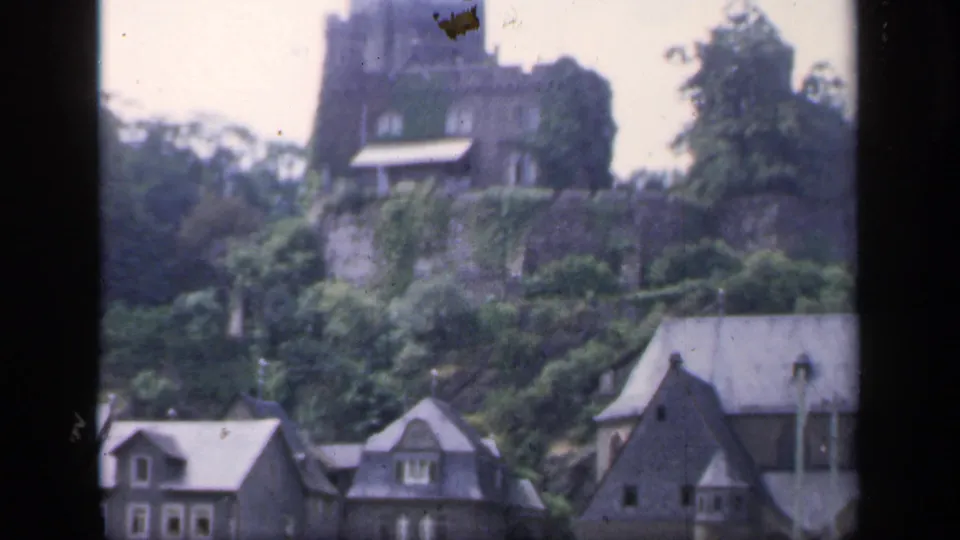 1949 Ireland frame with a castle-like structure, dense greenery, stone retaining wall, and village houses below.