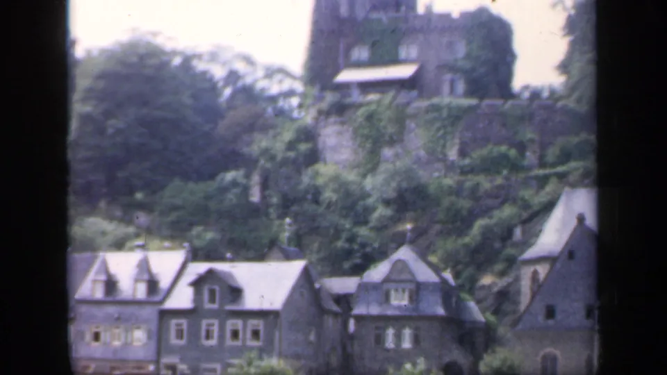 1949 Ireland home-movie view of dark-roofed village houses beneath a green hillside and castle-like stone tower.
