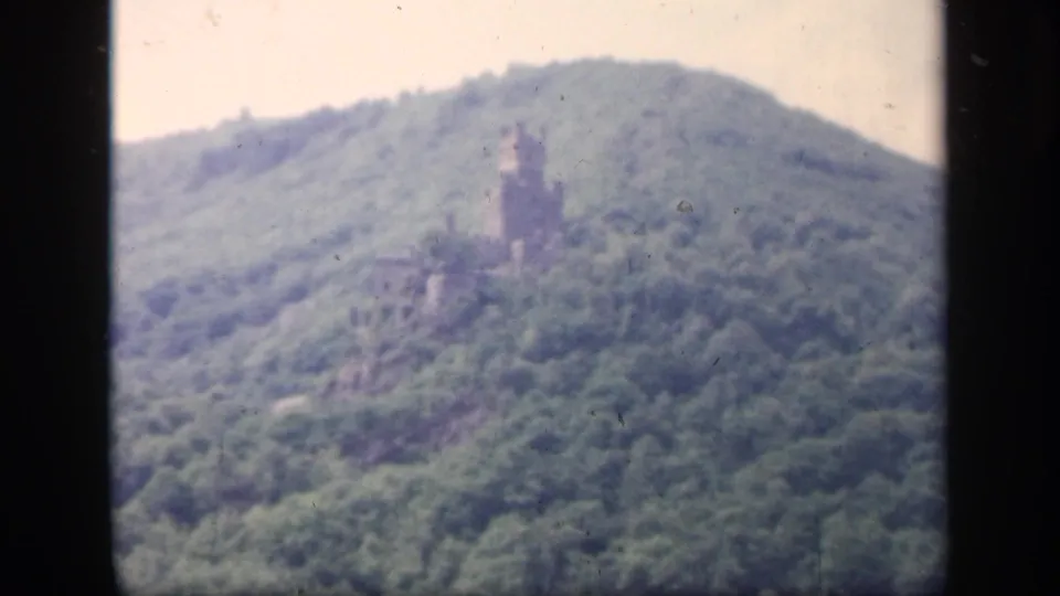 1949 Ireland 8mm frame showing a closer, soft-focus view of a castle-like stone ruin on a wooded hillside.