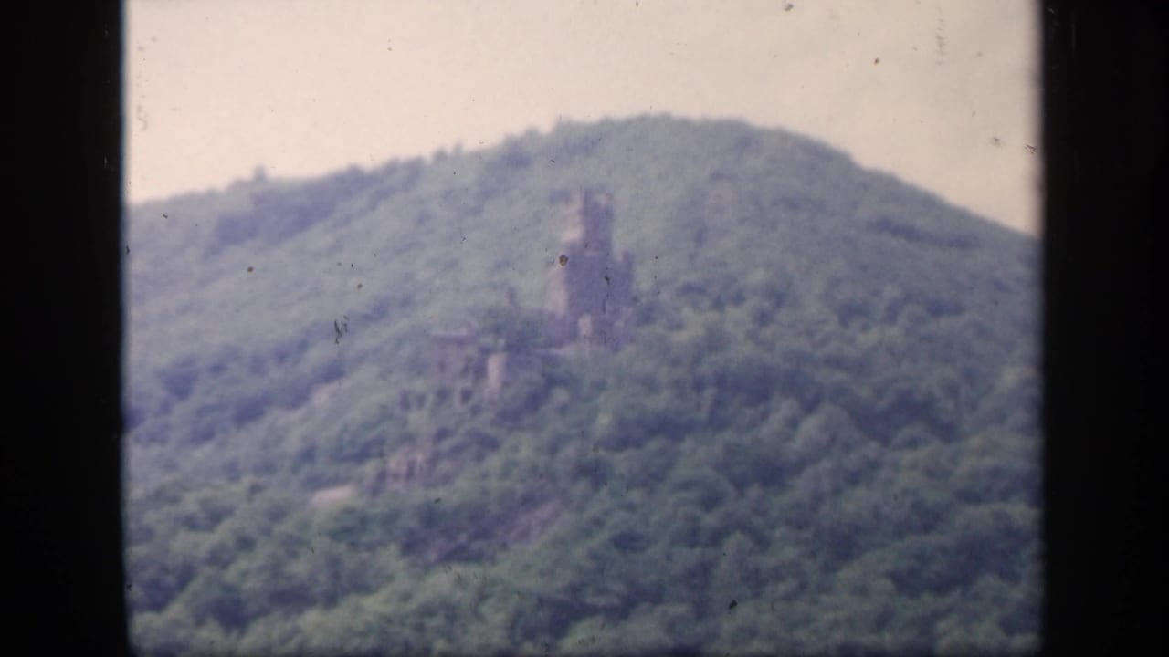 1949 Ireland 8mm frame showing a distant castle ruin or tower on a forested hill under a pale sky.