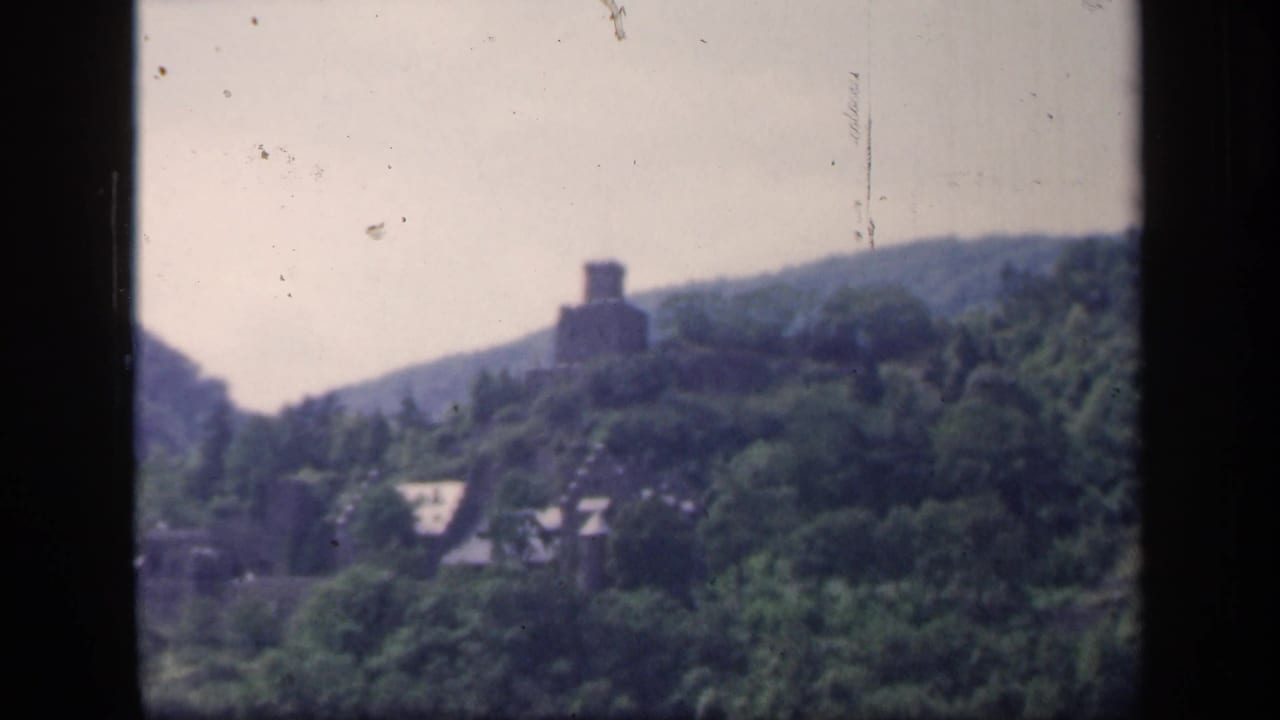 1949 Ireland 8mm frame showing a hilltop ruin above dense trees and small rooftops in a valley setting.